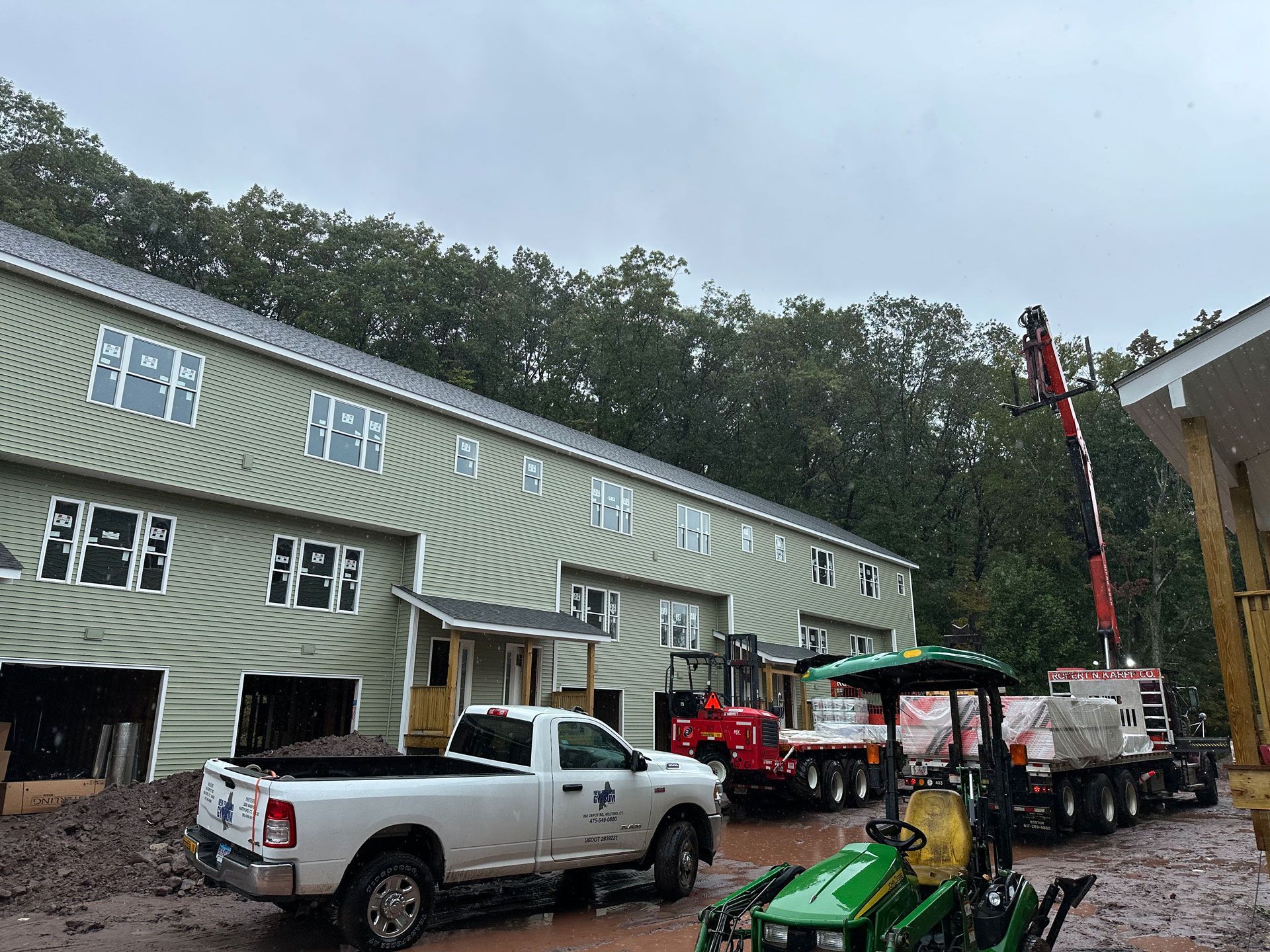 Workers and trucks outside a building during construction, with a crane and equipment in front.