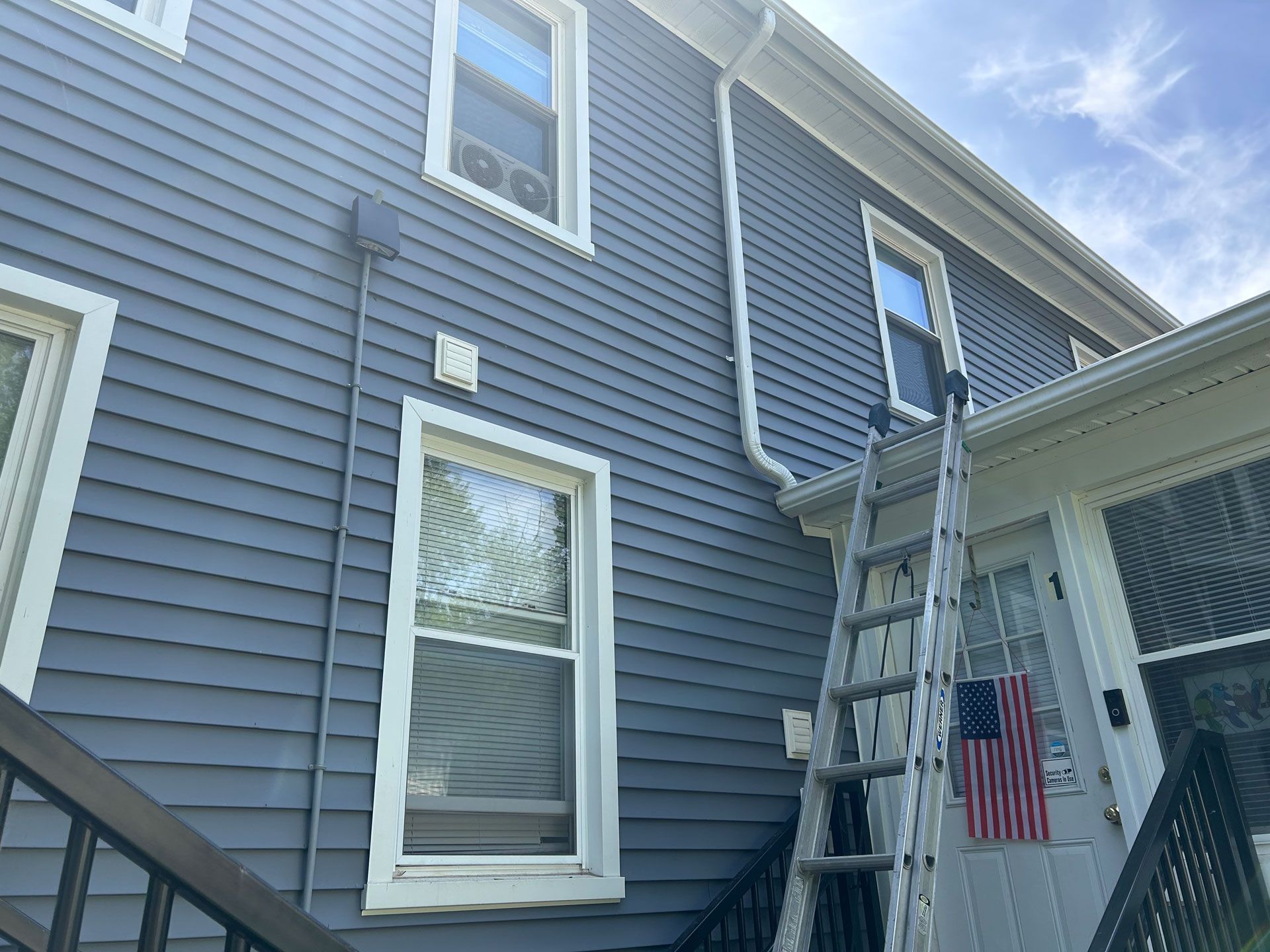 Blue house exterior with a ladder leaning against the siding near a porch and American flag
