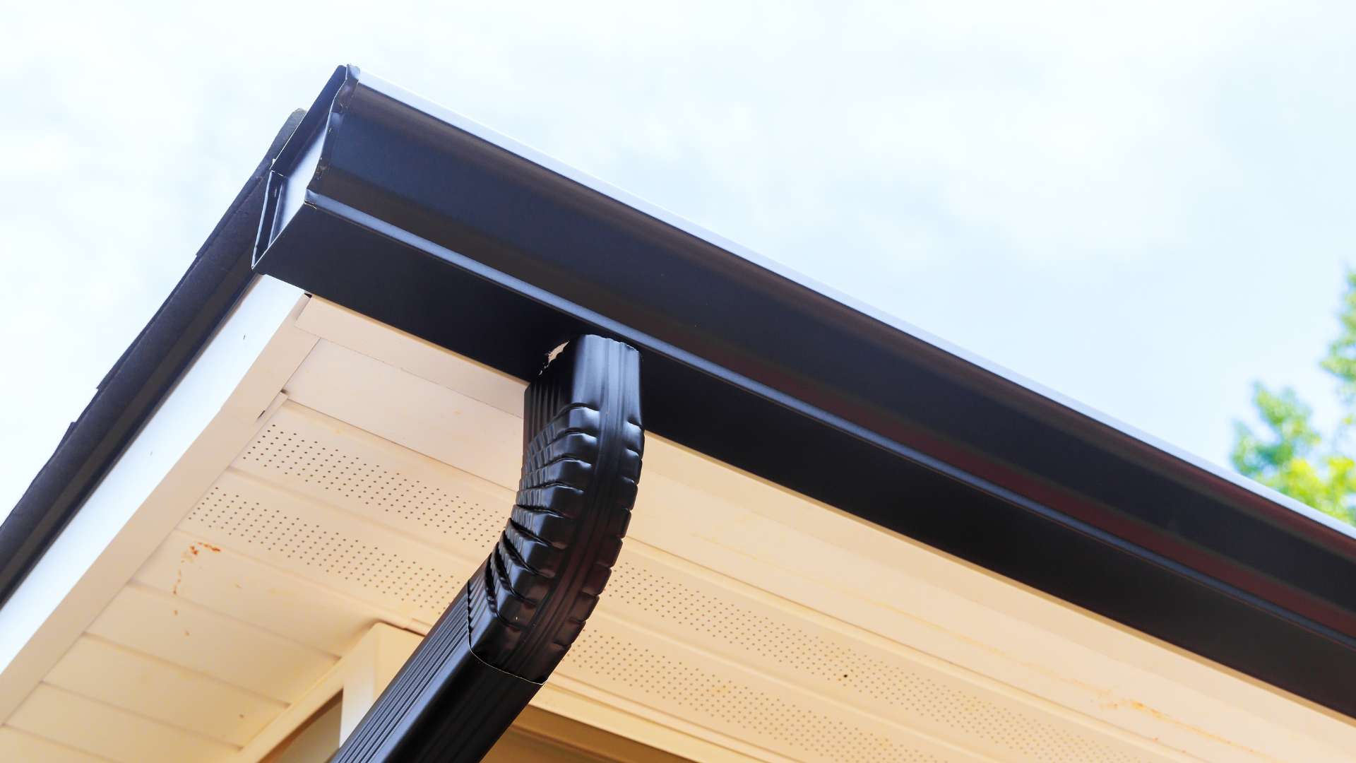 Close-up of a house roof eave with a black gutter against a bright sky