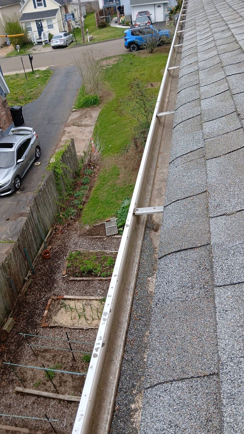 View from a roof gutter over a sloped shingle roof to a backyard and driveway below