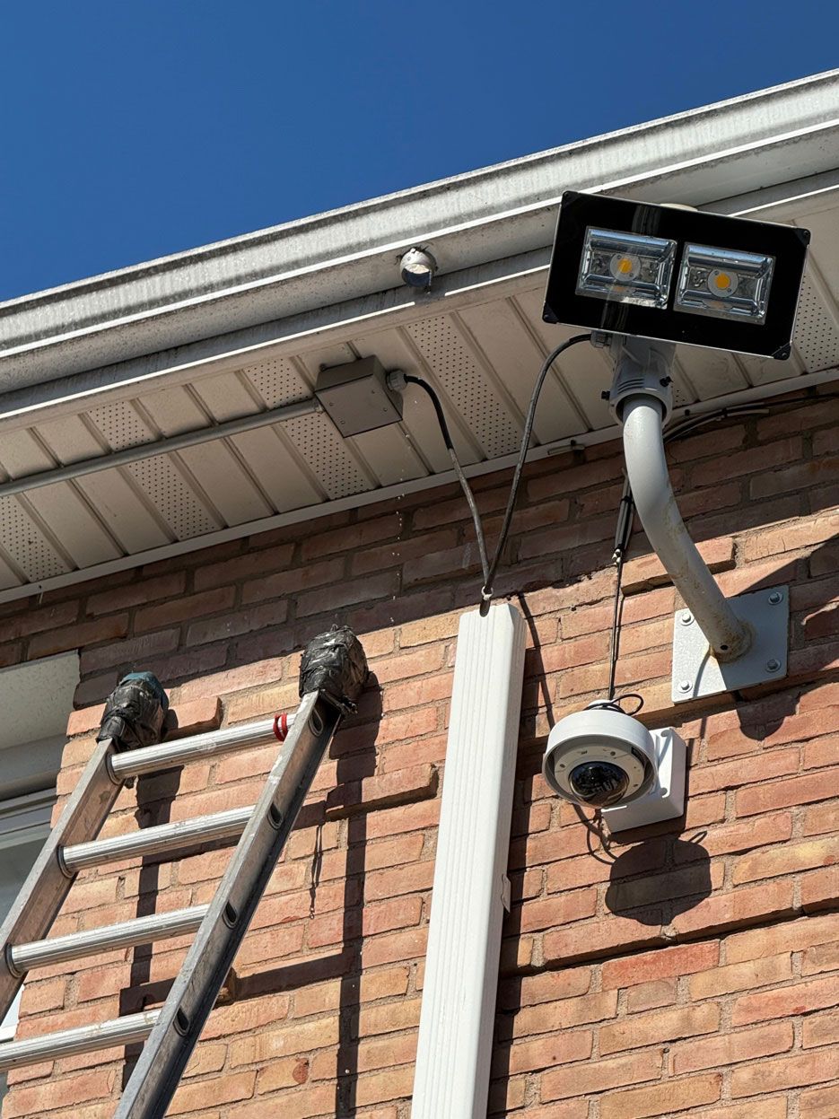 Security camera and floodlight mounted on a brick house under the roofline.
