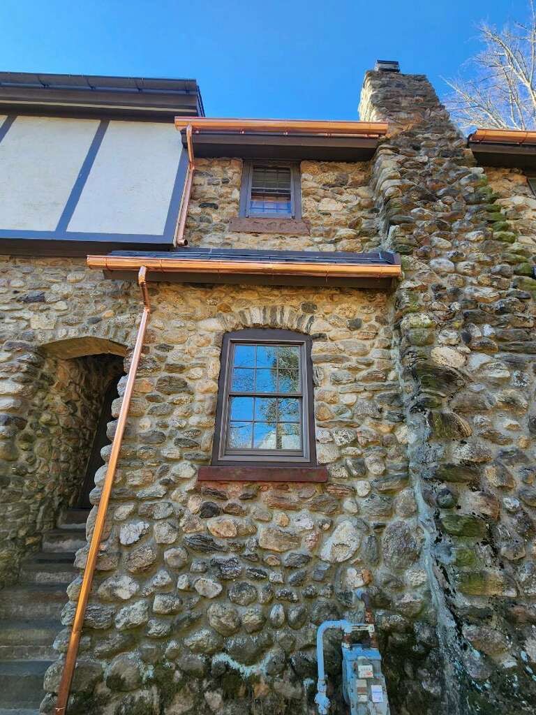 Stone cottage facade with blue-framed windows, wooden trim, and a stone chimney under a bright sky