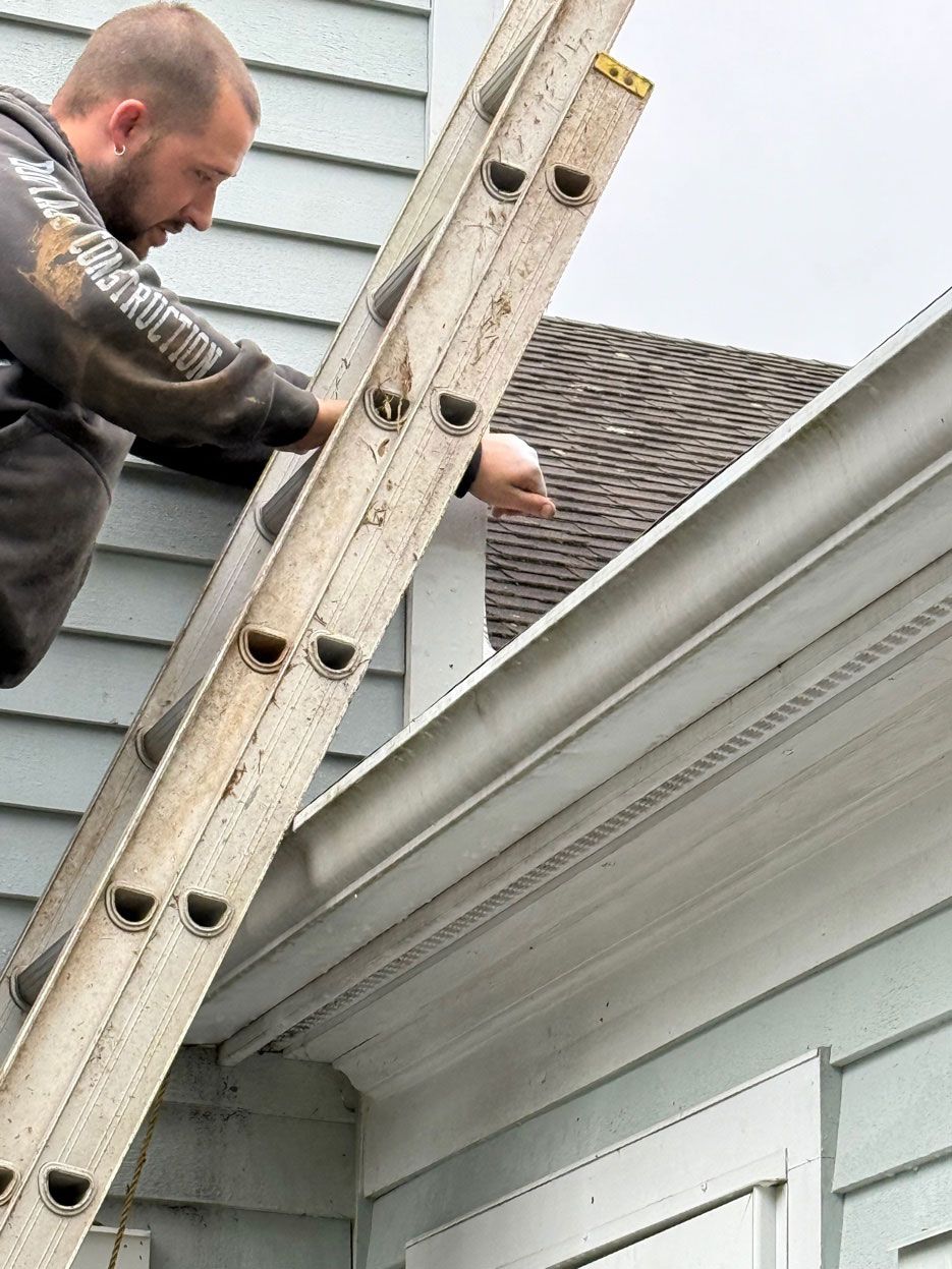 Man on a ladder repairing a house roof gutter