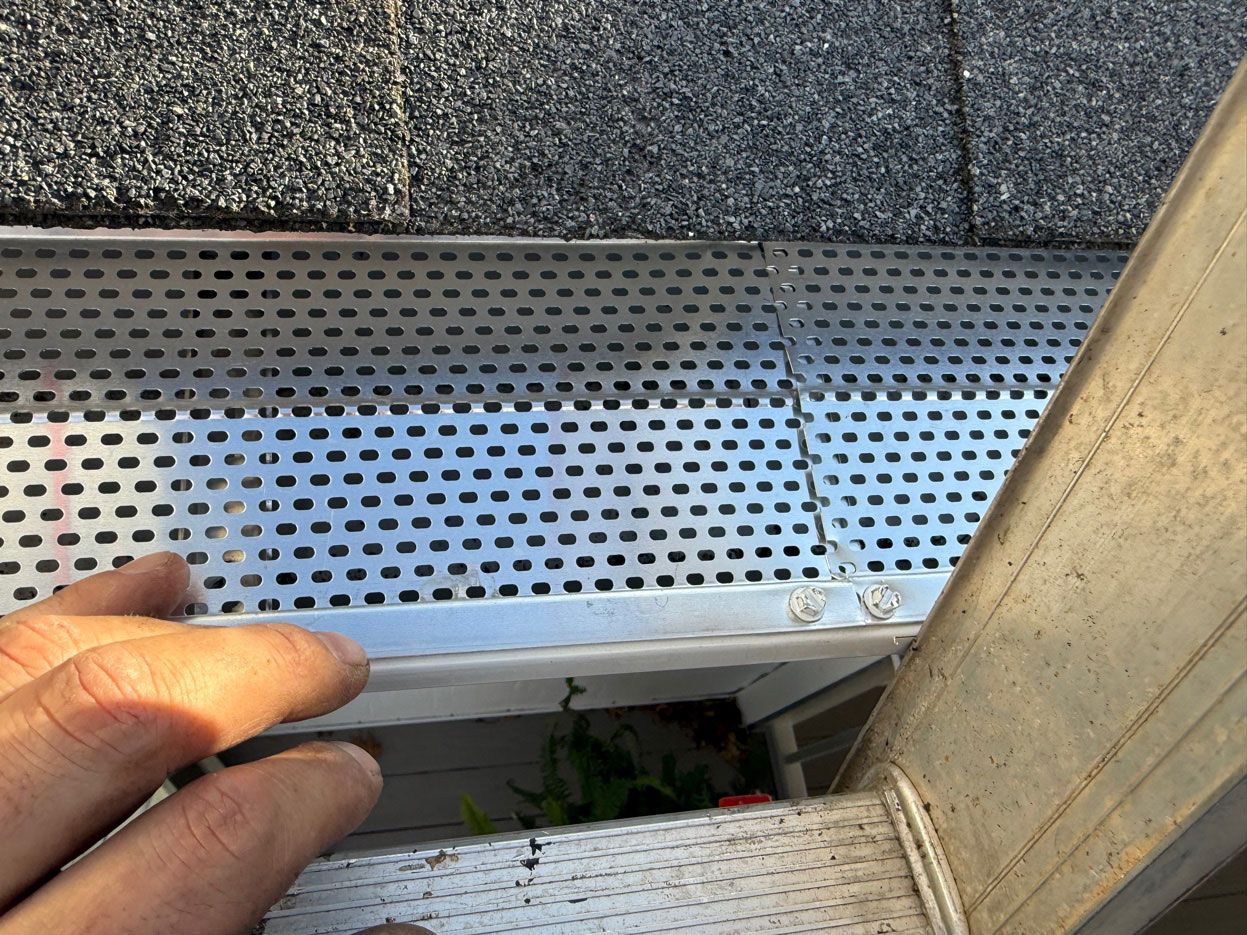 Hand holding a white gutter downspout near a metal roof edge and perforated drain panel