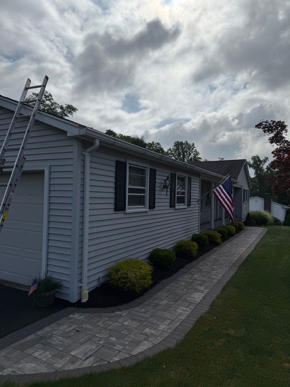 Single-story gray house with white shutters, stone walkway, and American flag under cloudy sky