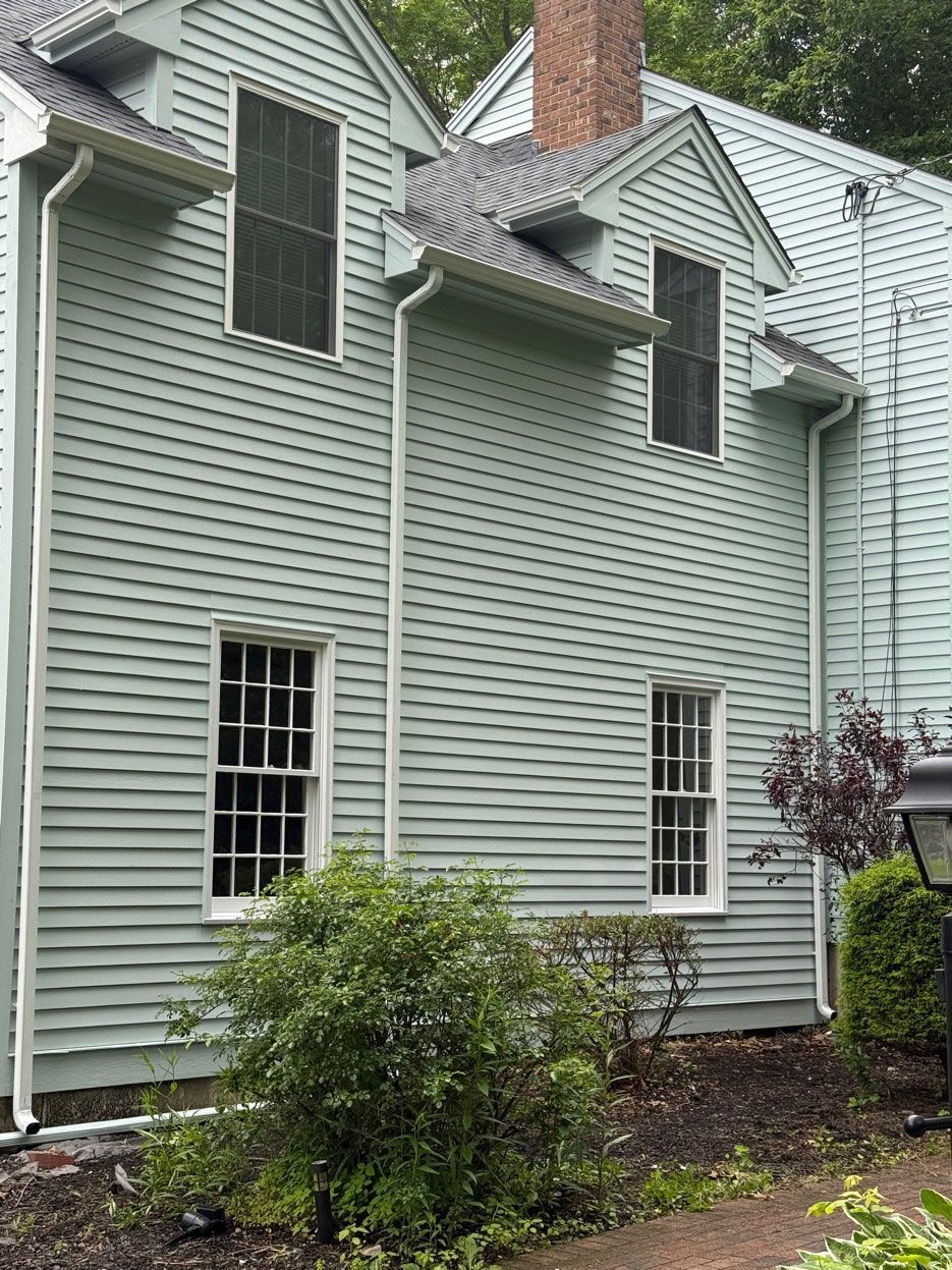 A hand presses down on a perforated metal gutter guard installed over a white rain gutter below dark roof shingles.