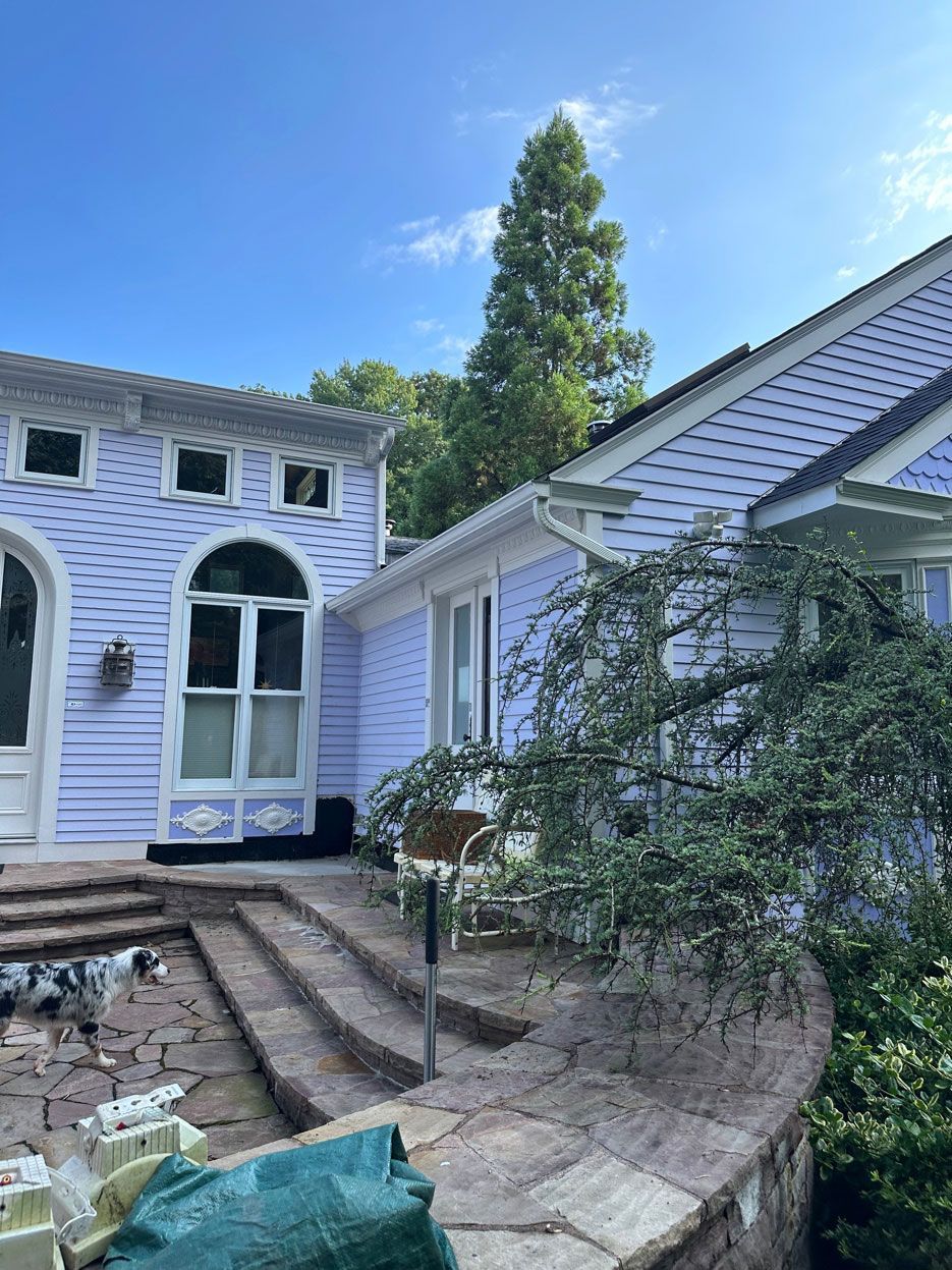 Stone steps leading to a lavender house and white building with arched windows, under a blue sky.