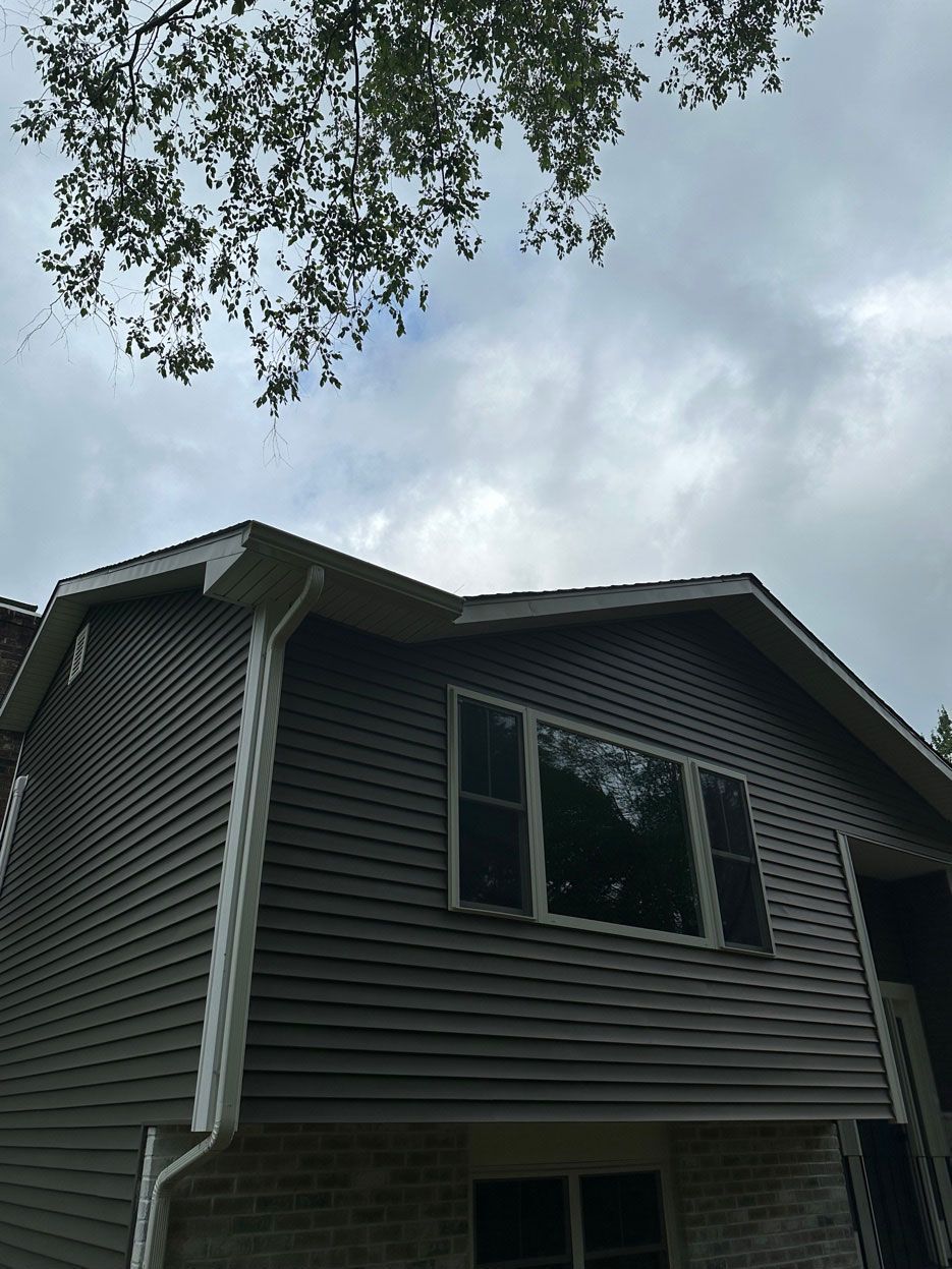 Exterior of a gray house with a second-floor window under an overcast sky