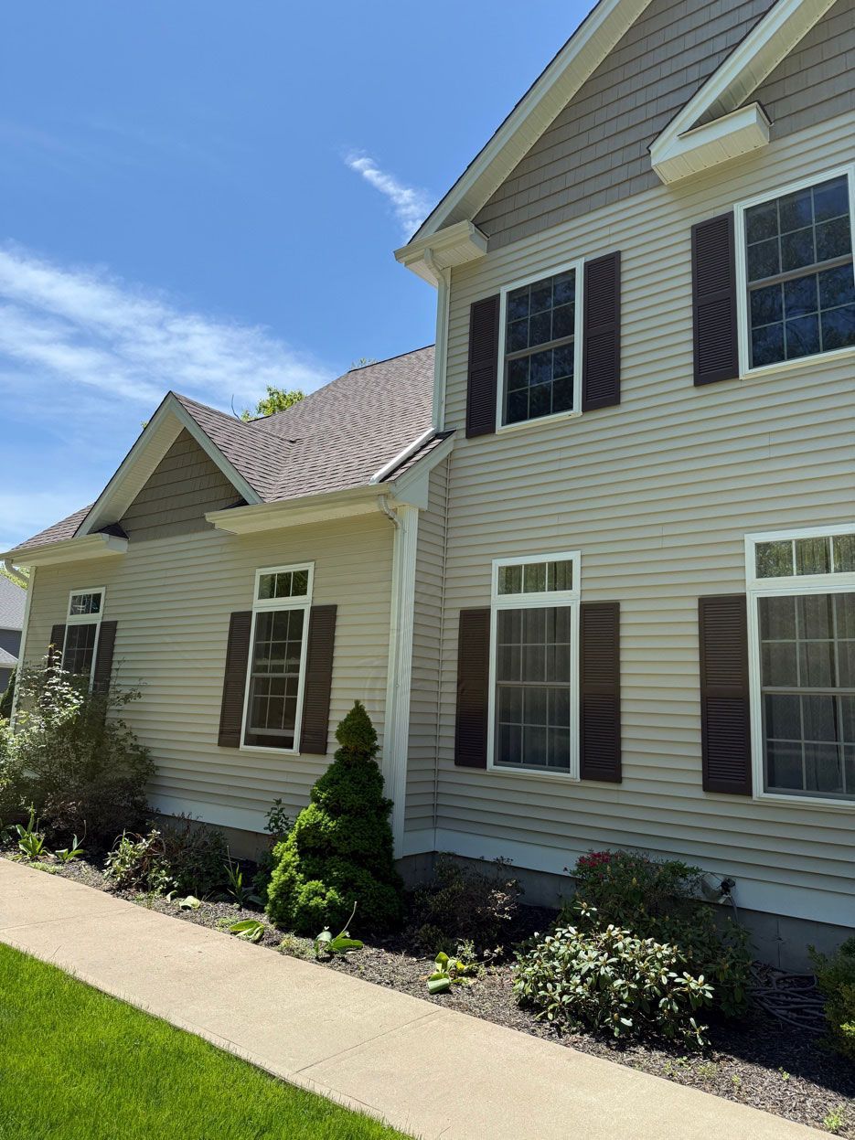 Suburban house exterior with beige siding, brown shutters, and a front walkway under a blue sky