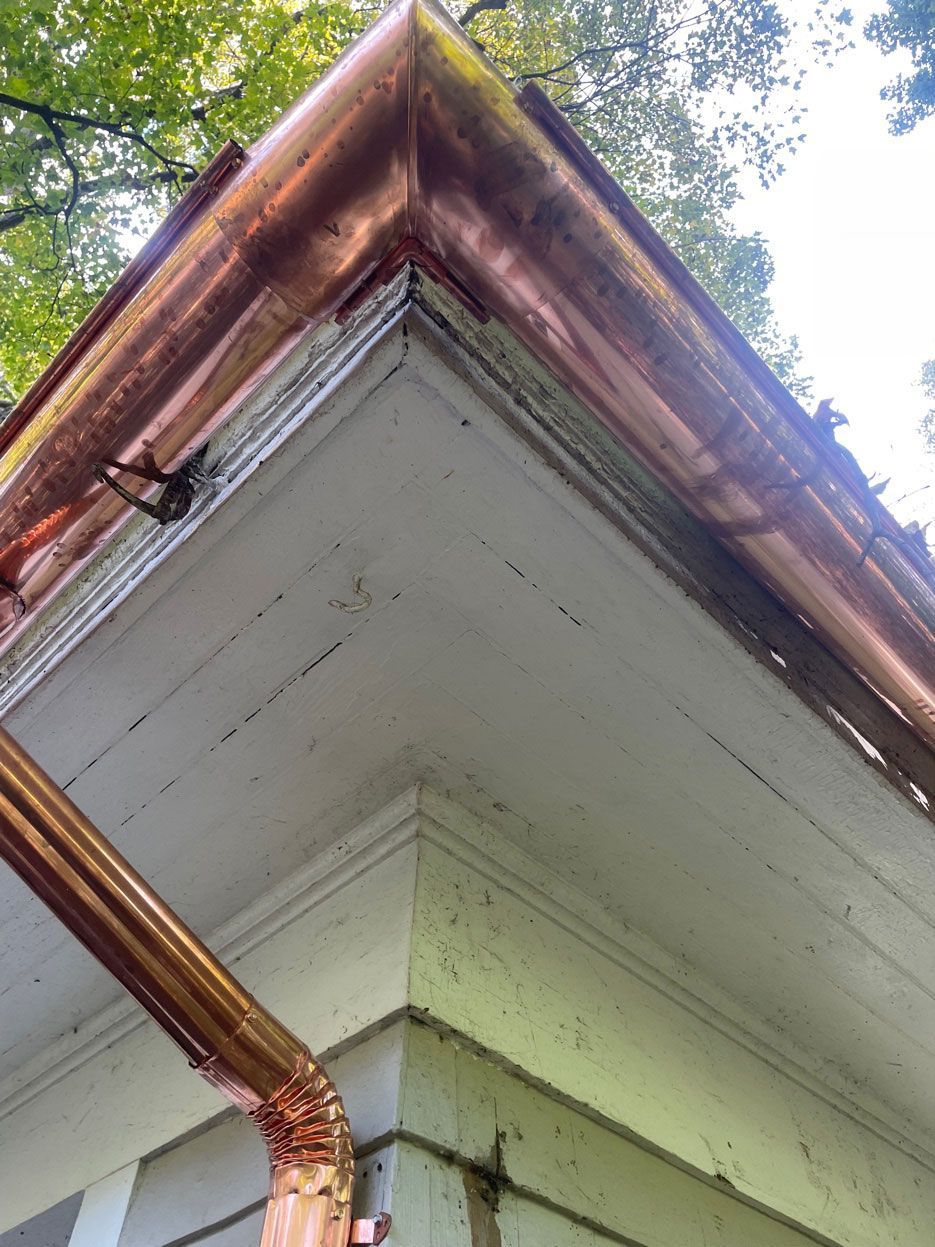 Copper gutter and downspout on a white house corner beneath trees