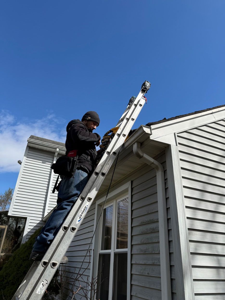 Person working on a ladder beside a house roof under a clear blue sky