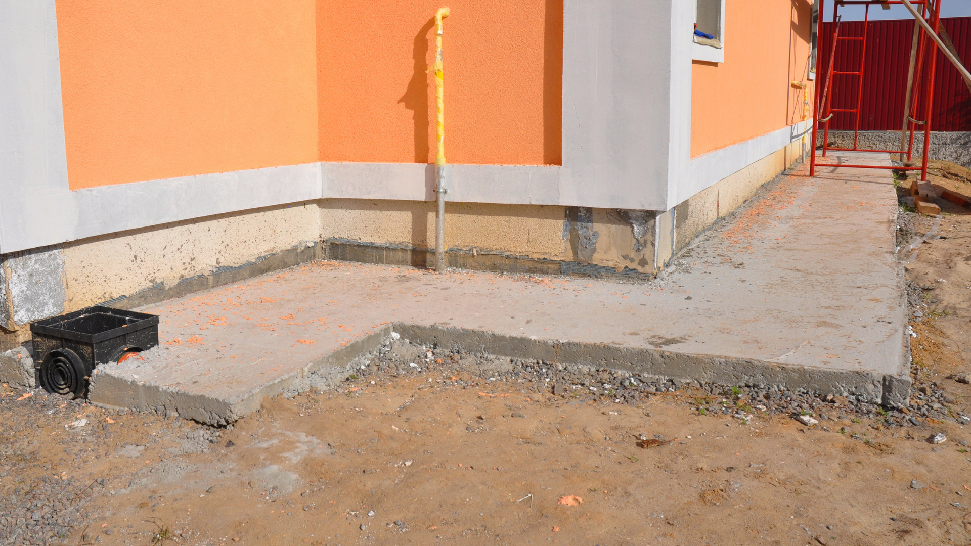 Ramp and walkway beside an orange building, with a small step and rough concrete path.