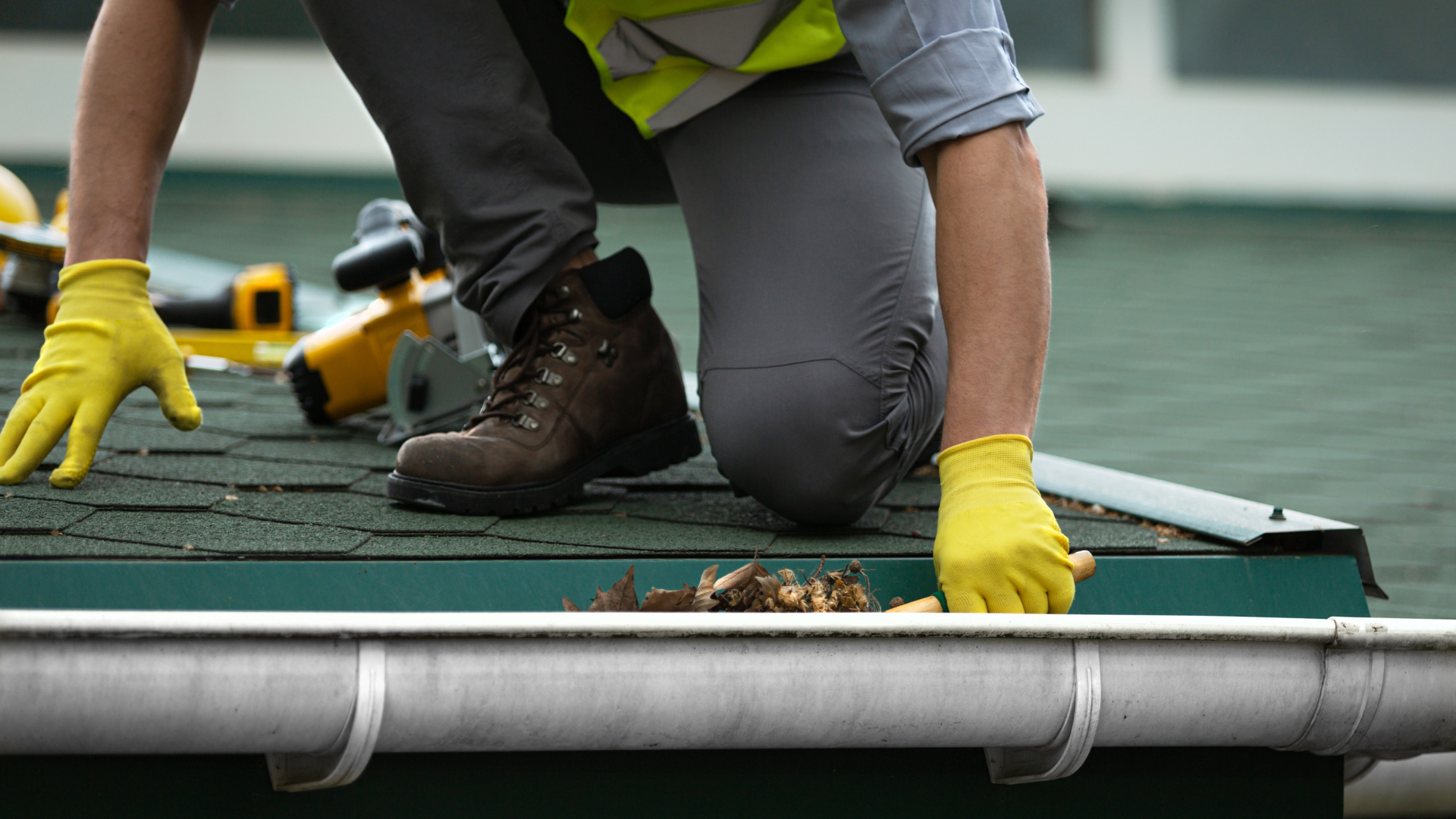 Worker in yellow gloves installing a green roof membrane on a rooftop.