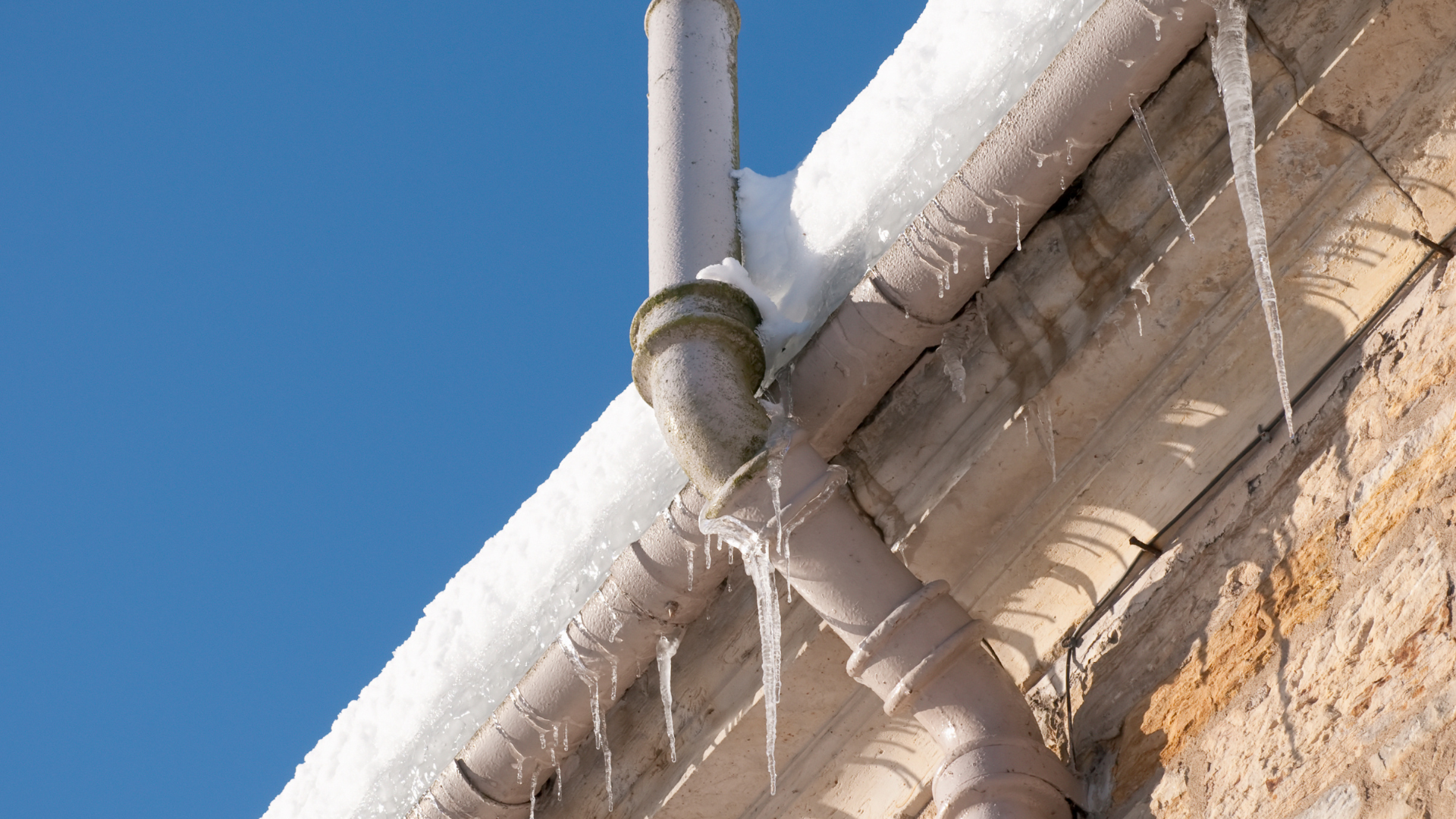 White drainage pipes along a tan brick wall under a clear blue sky