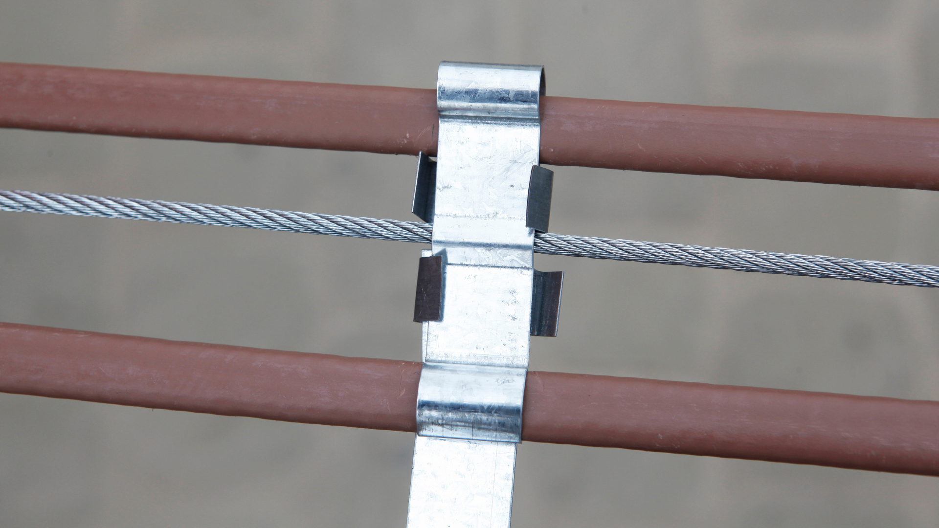 Close-up of a metal cable clamp securing braided wire between two brown rails