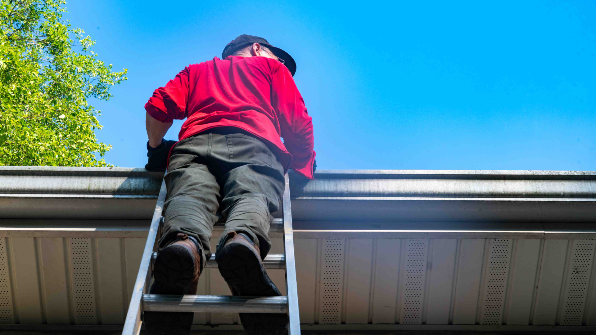 Person in a red jacket climbing a ladder onto a roof under a blue sky