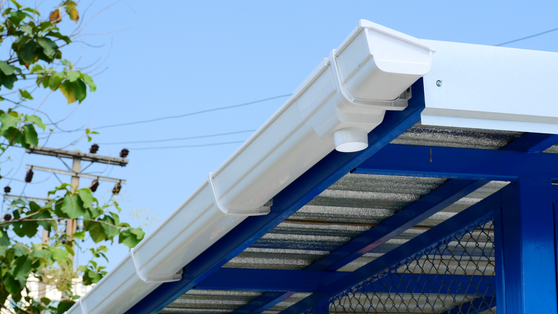 Blue-and-white roof eaves with metal mesh underside against a clear sky, with tree branches at left