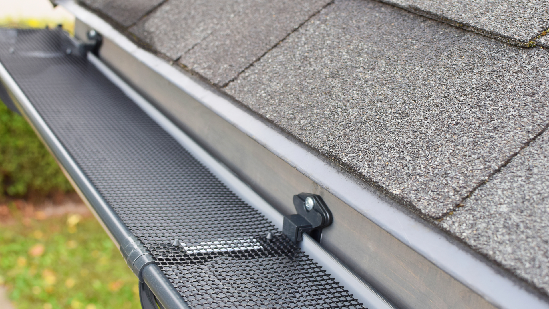 Roof gutter guard along gray shingle roof edge with a black clip and fastener