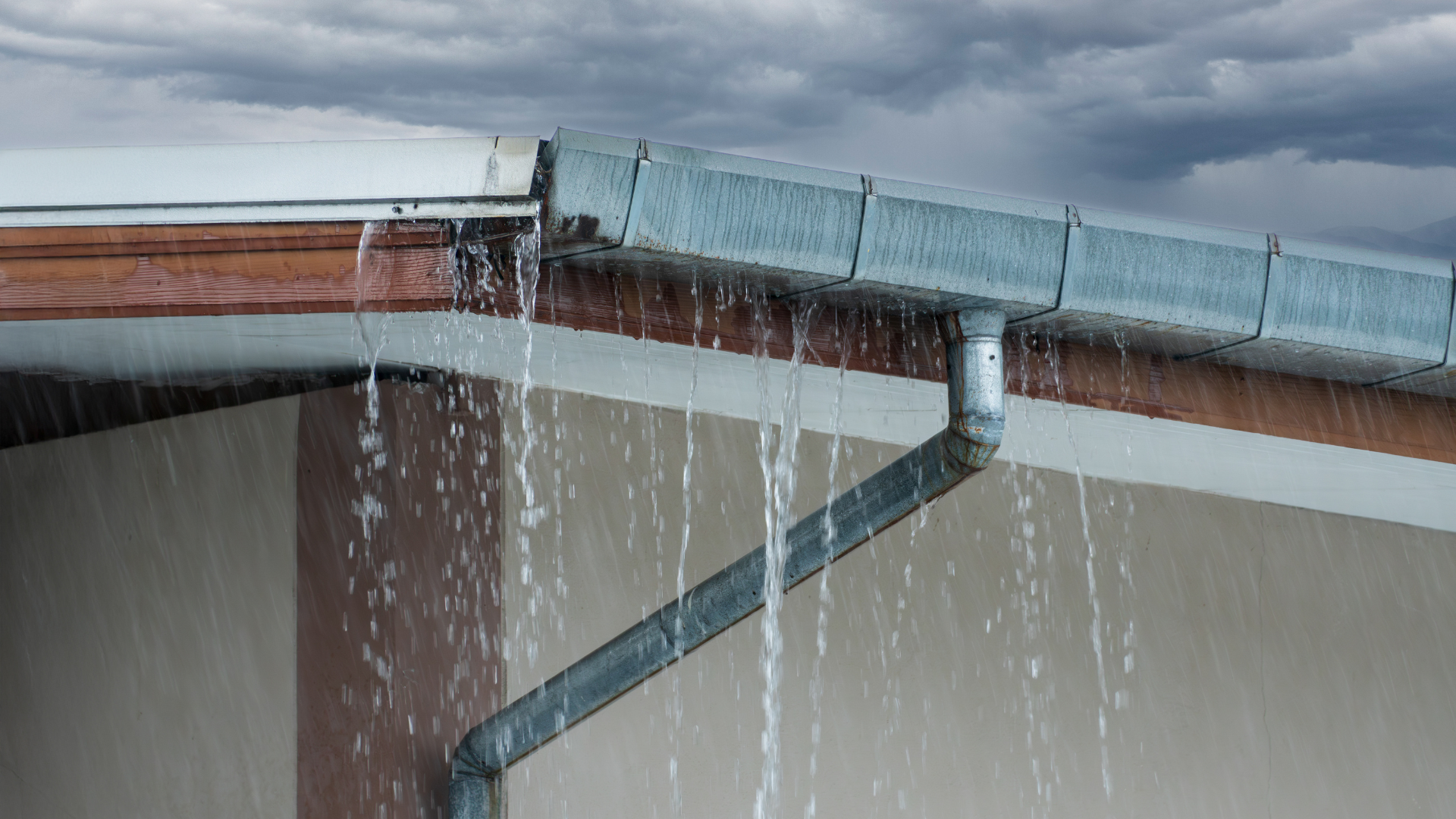 Overflowing rain gutter pouring water off a roof onto a downspout during heavy rain