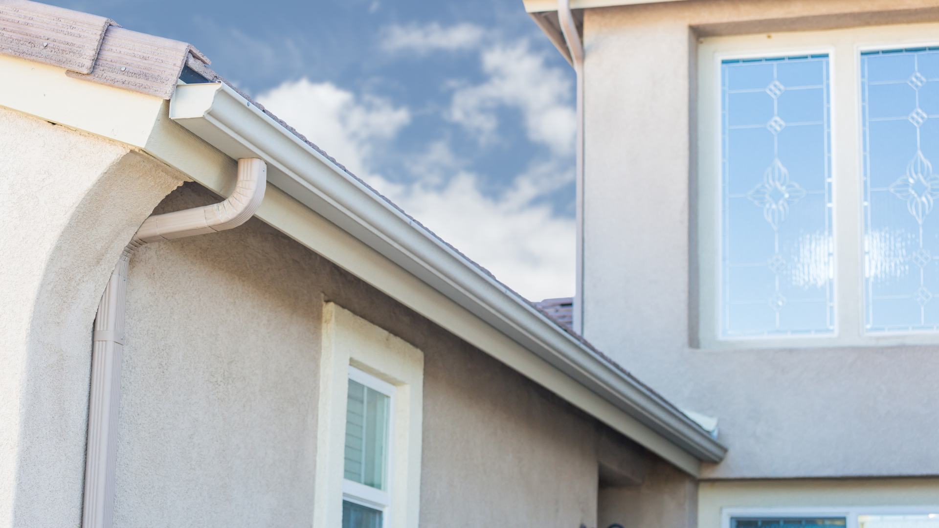 White stucco house exterior with roof eaves and a window under a blue sky