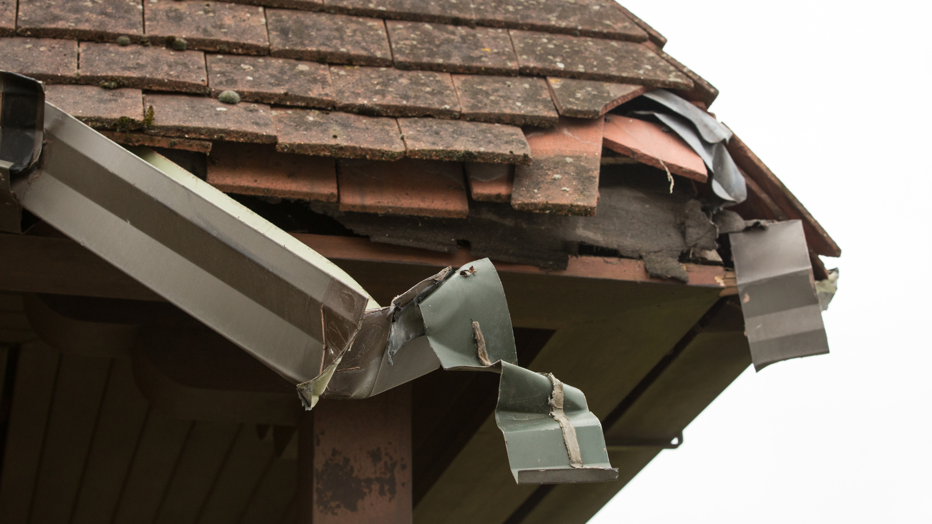 Damaged roof corner with broken brown shingles and bent white gutter