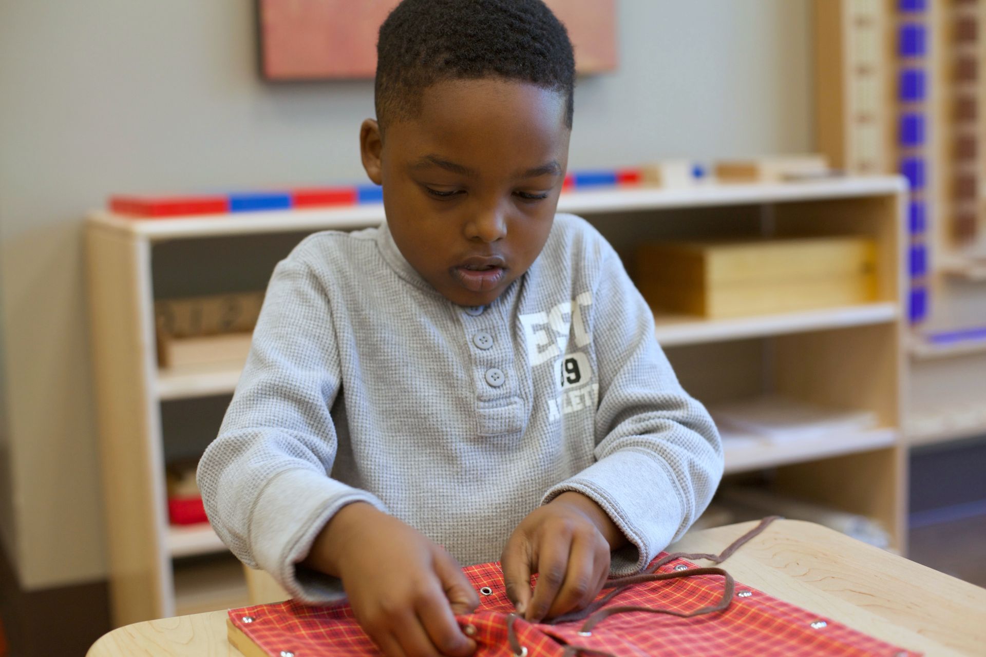 Child in a classroom working on the lacing frame at a table.