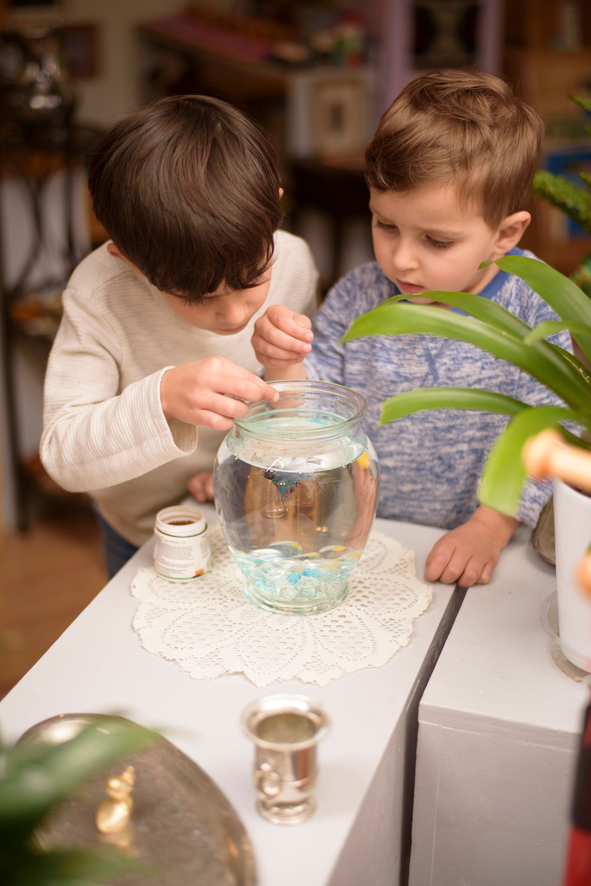 Two children feeding fish at a table indoors