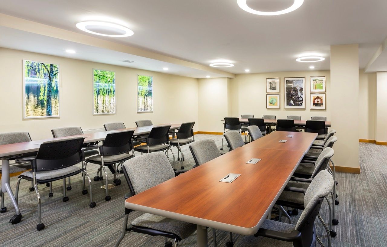 Conference room with long wood tables and gray upholstered chairs in a well-lit community space.
