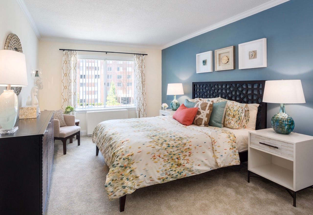 Bright bedroom in an apartment with a queen bed, blue accent wall, and matching lamps.