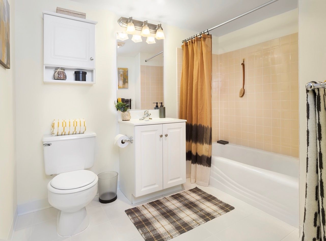 Bright bathroom with white vanity, toilet, and beige-tiled tub/shower.