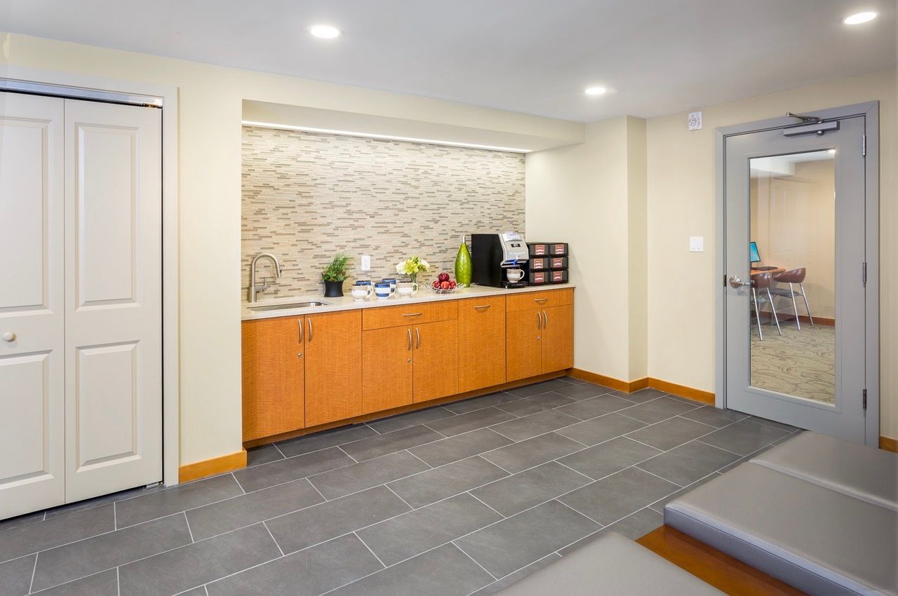 Communal kitchenette in a multifamily lobby with a sink, backsplash, and coffee station.