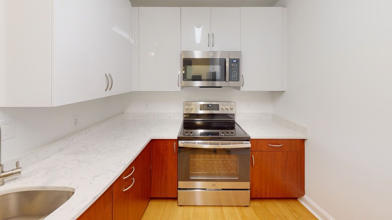 Kitchen with white upper cabinets, wood lower cabinets, and stainless steel stove and microwave.