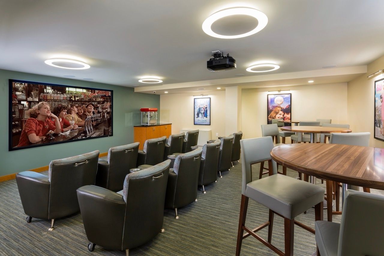 Indoor resident lounge with rows of black chairs, round tables, and circular ceiling lights.