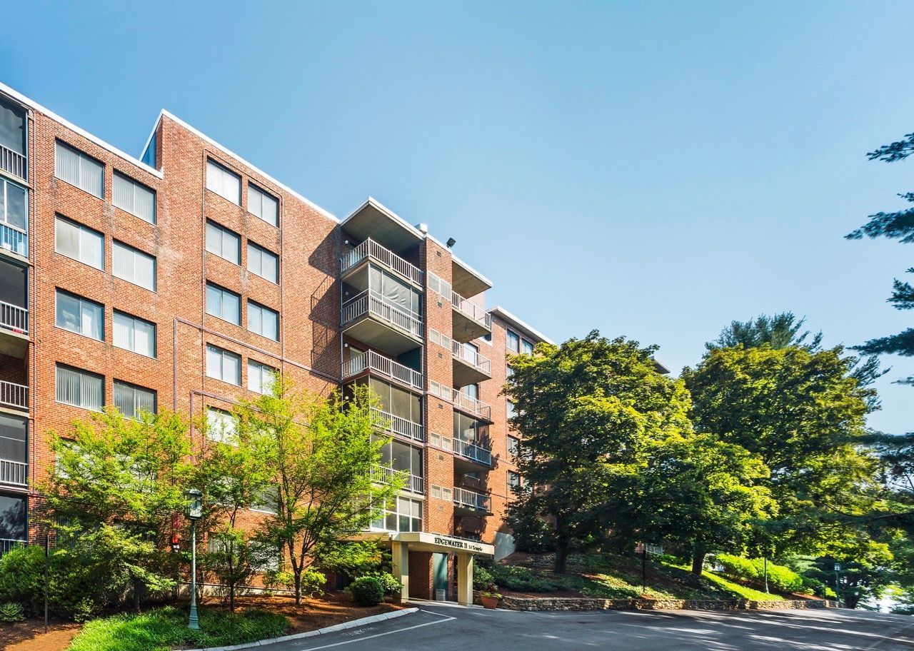 Exterior view of a brick apartment building with balconies, trees, and a clear blue sky.