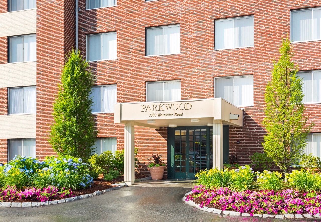 Entrance to a brick apartment building with a beige canopy and landscaped flower beds.