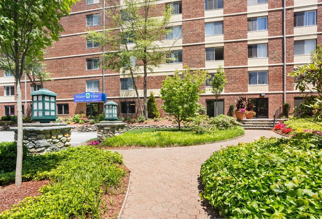 Exterior view of a brick apartment building with a landscaped courtyard and brick walkway.