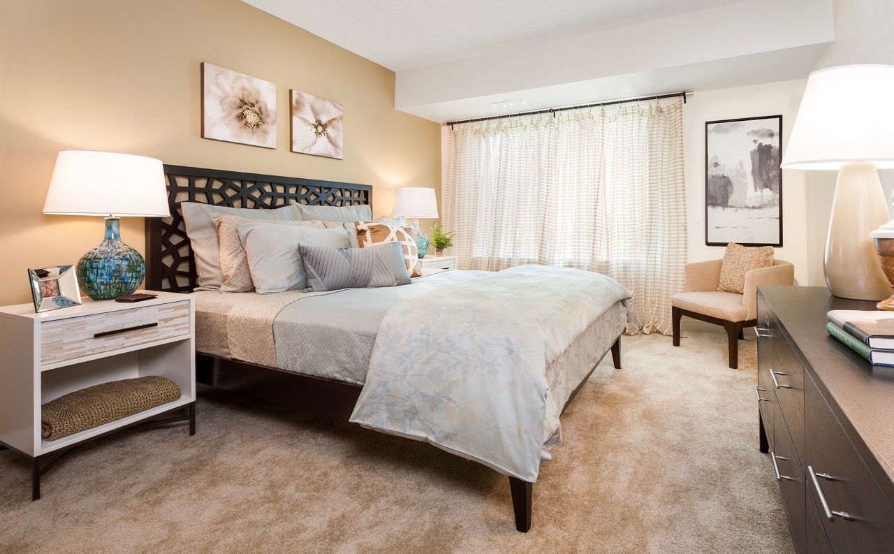 Bedroom in a modern apartment with a large bed, upholstered headboard, and two nightstands.