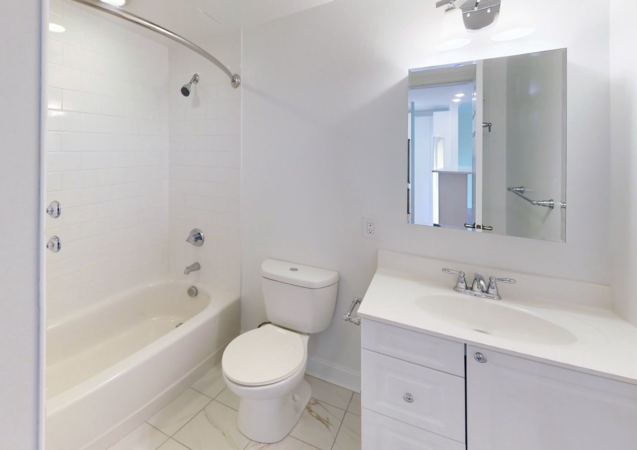 White bathroom with tub/shower, toilet, and a white vanity with mirror.