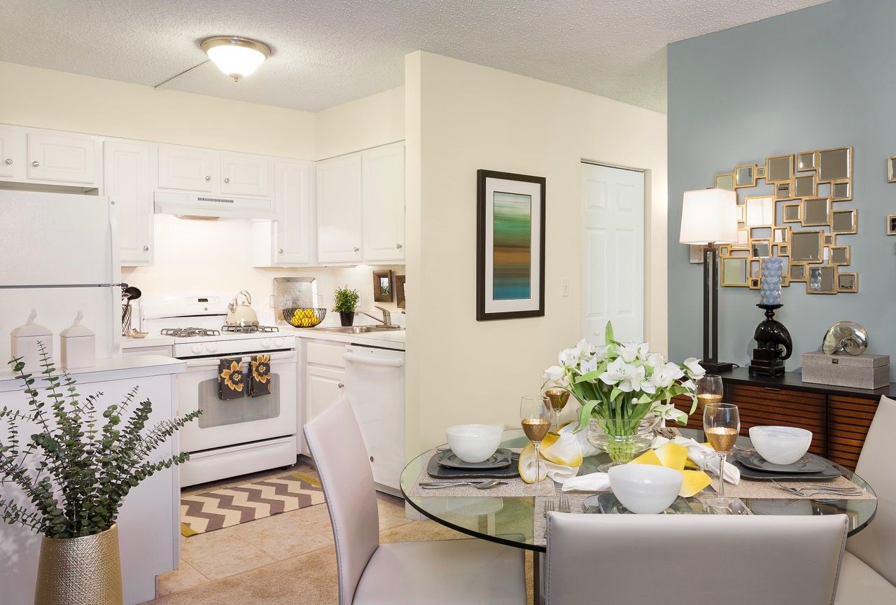 Open-concept apartment kitchen with white cabinets and a glass dining table.