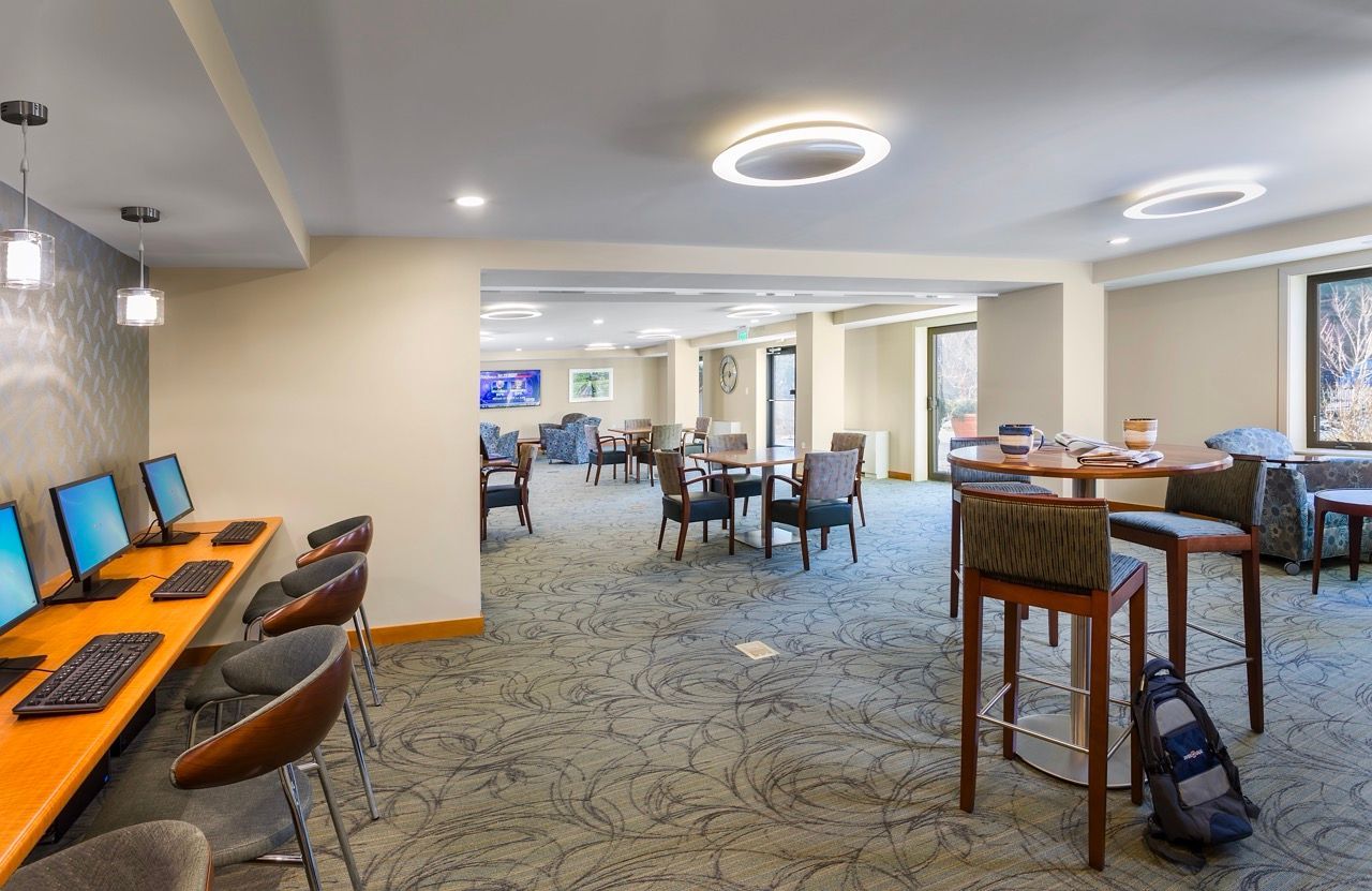Indoor community lounge with computer desks, round tables, and seating.