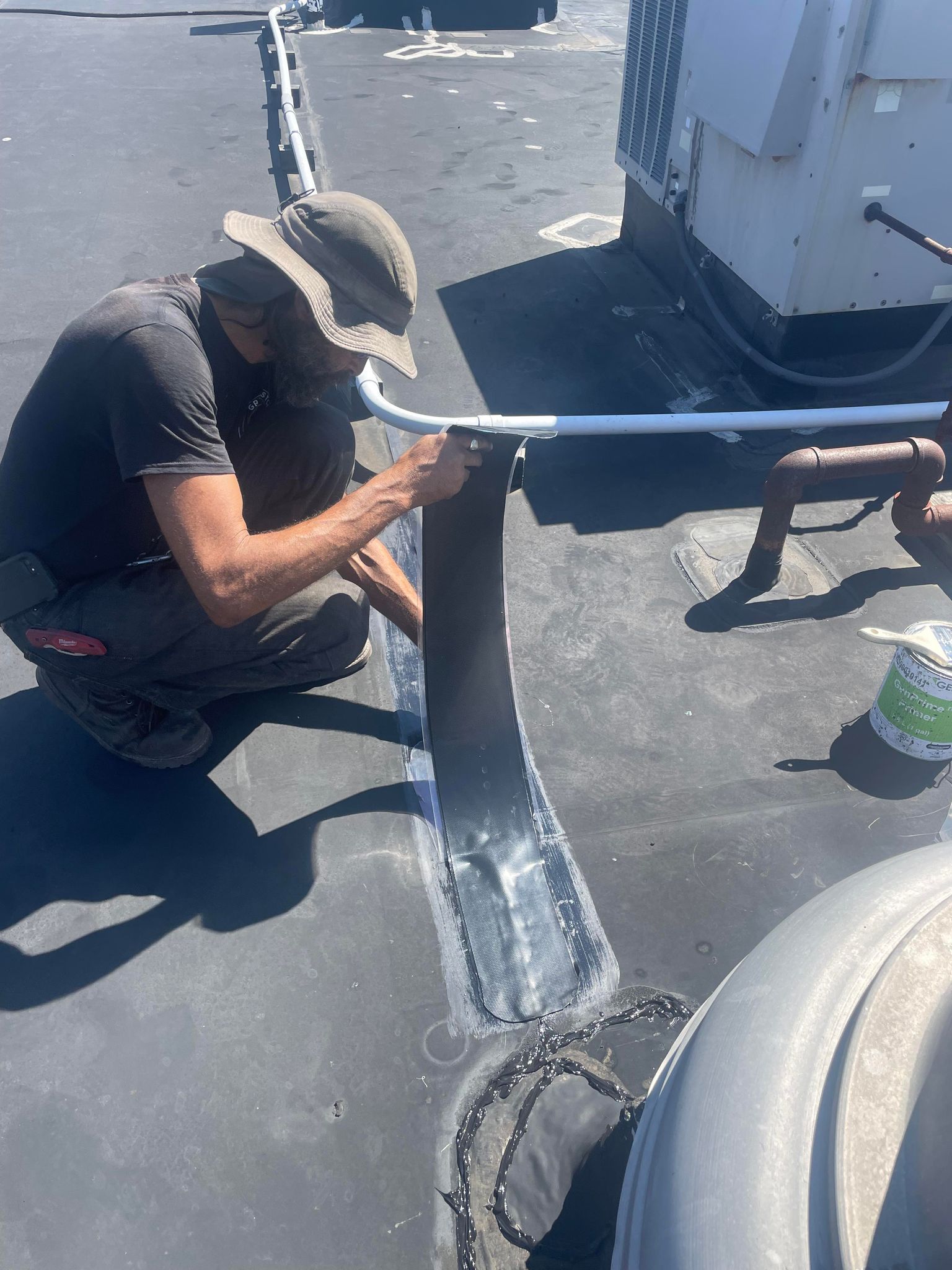 Man repairing roof seam with sealant on a rooftop.