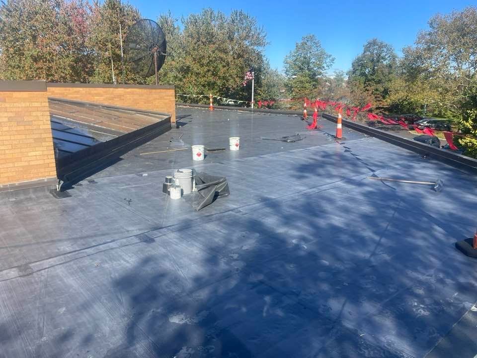 Flat roof under construction with dark membrane, buckets, and safety cones.