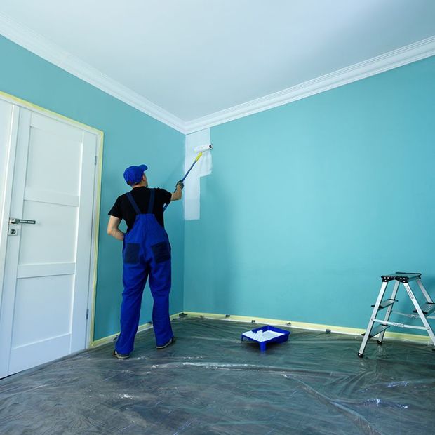 Painter in blue overalls painting a white stripe near the ceiling of a teal-walled room. Painter in blue overalls painting a white stripe near the ceiling of a teal-walled room.
