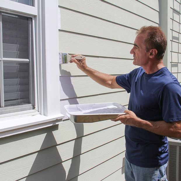 Man painting exterior trim of a house with a paintbrush and paint tray. Man painting exterior trim of a house with a paintbrush and paint tray.