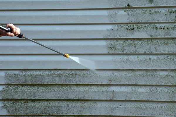 Pressure washing a section of moldy white siding, showing cleaned and dirty areas.