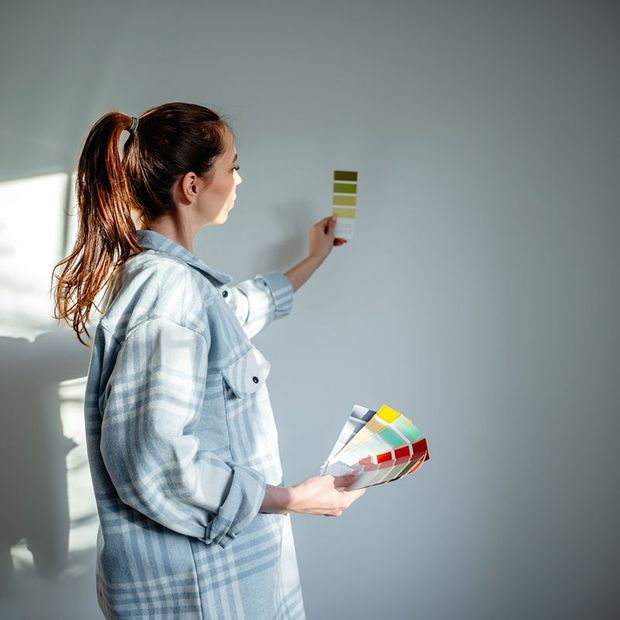Woman holding paint swatches, comparing colors on a white wall. Woman holding paint swatches, comparing colors on a white wall.