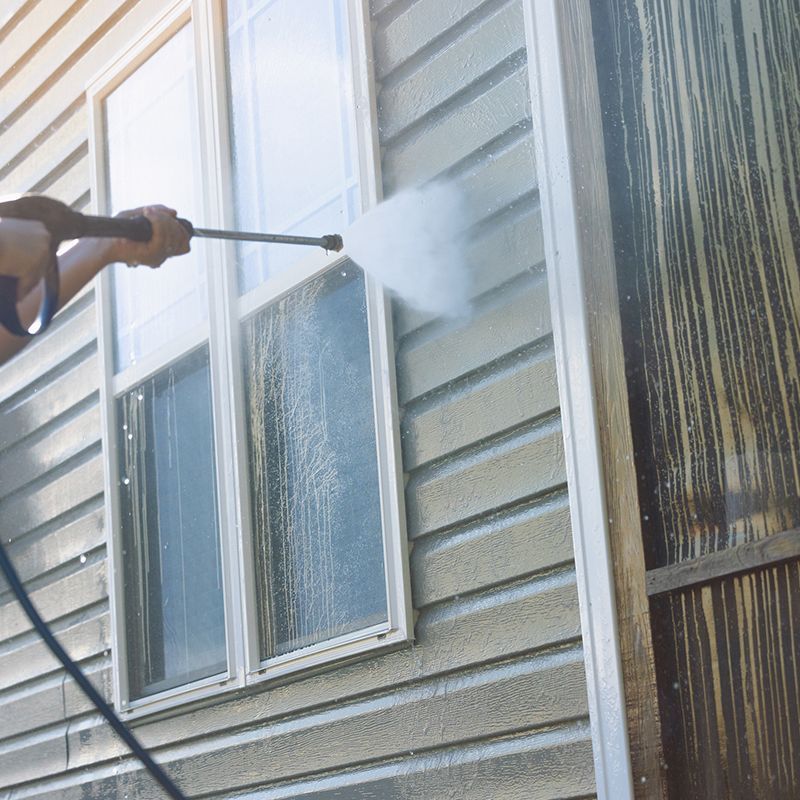 Person using a pressure washer to clean siding near a window. Dirty streaks on the siding are visible. Person using a pressure washer to clean siding near a window. Dirty streaks on the siding are visible.