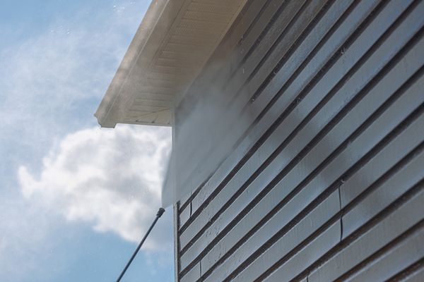 Power washing siding on a house; steam and cloudy sky.