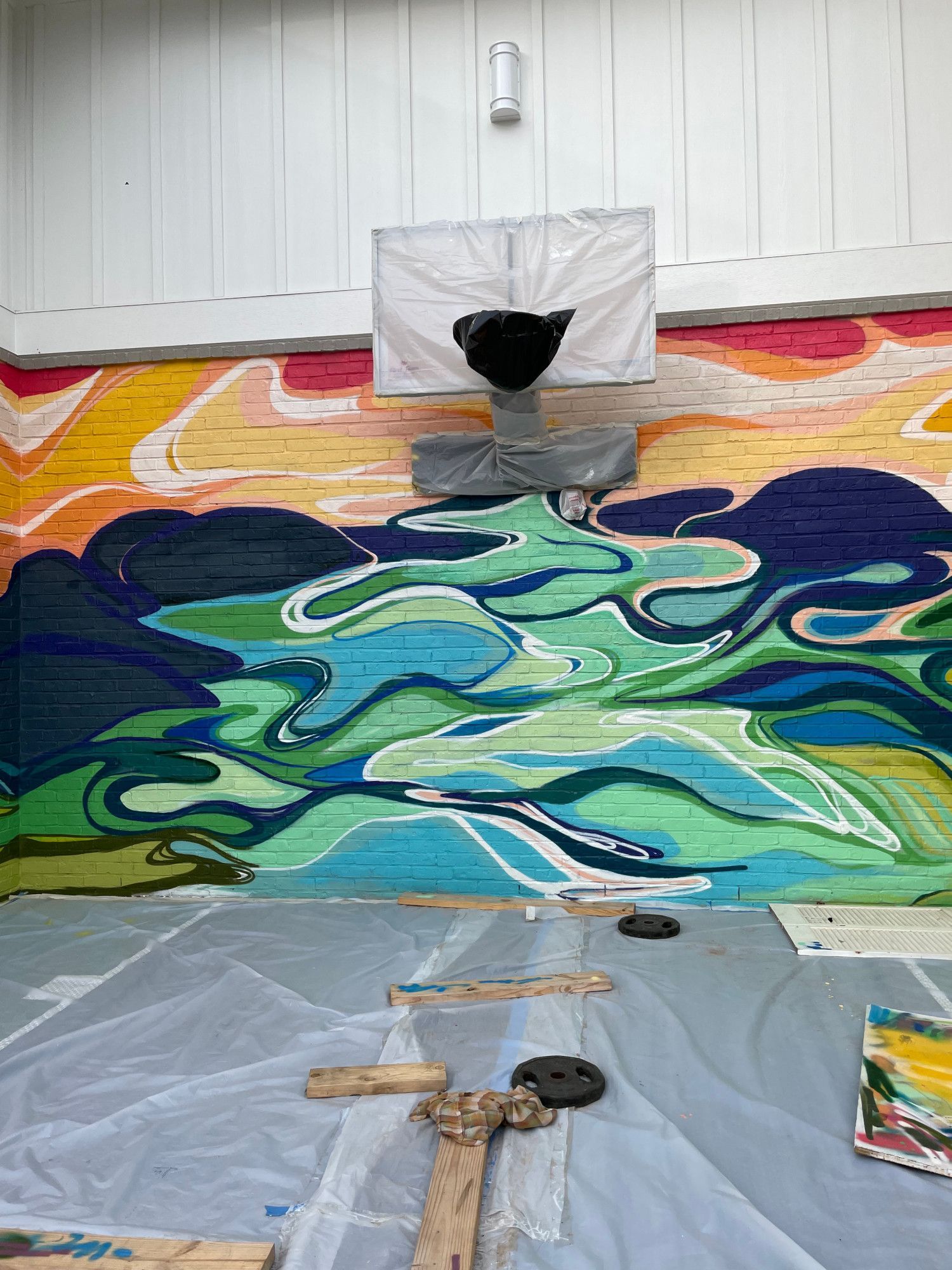 Abstract mural depicting a landscape in blue and green hues. A plastic sheet covers the floor with wooden planks.