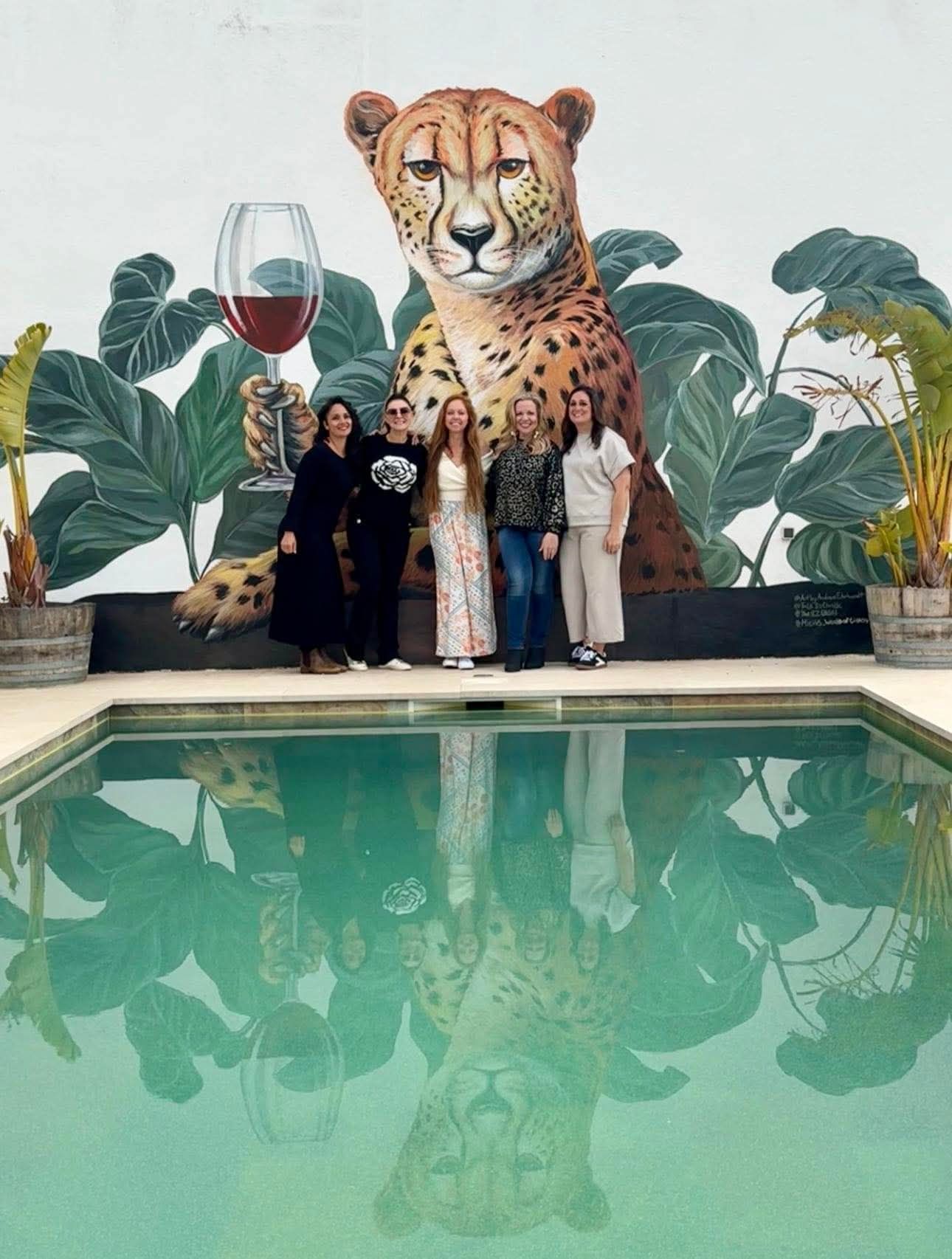 A group of people standing in front of a mural of a cheetah holding a glass of wine